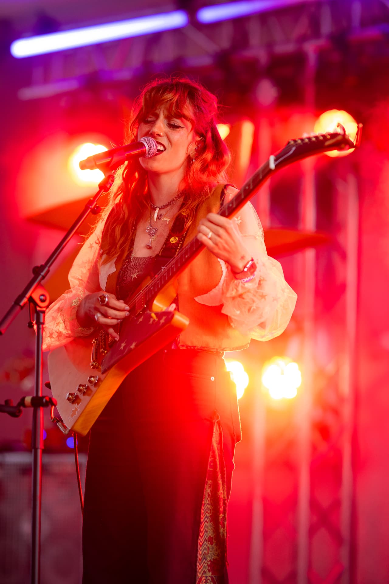 Gini Brown – Rothaarige Sängerin singt ins Mikrofon und spielt E-Gitarre mit Sternenverzierungen im roten Bühnenlicht