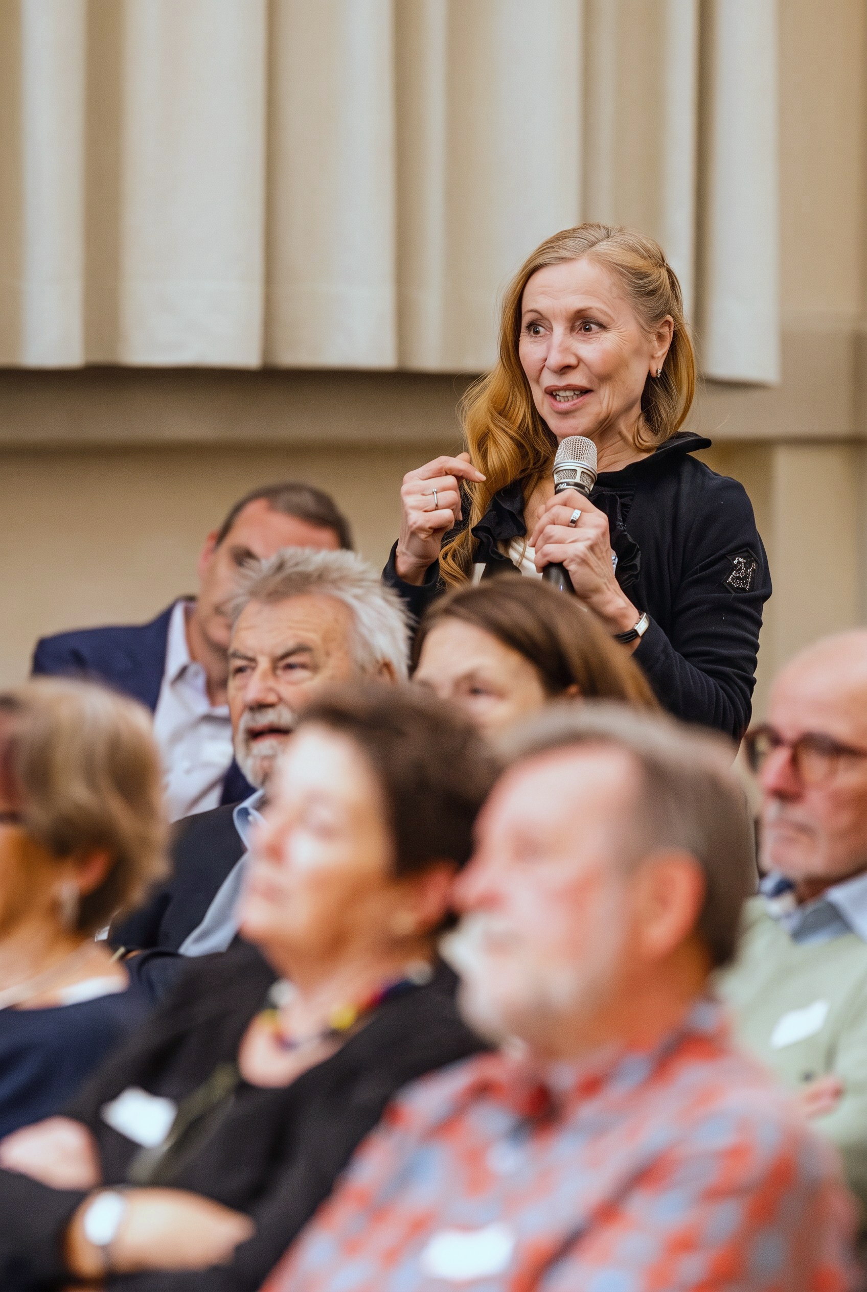 A woman with a microphone speaking from the audience at an event