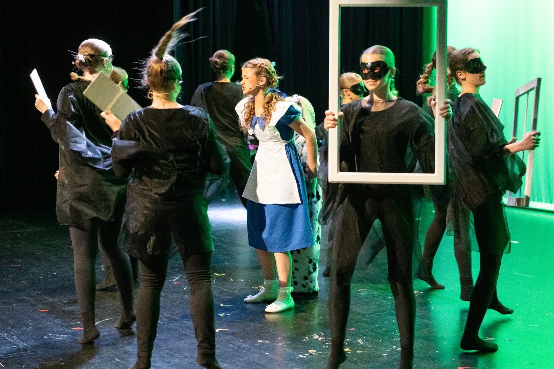 Dorothy, umringt von Darstellerinnen in schwarzen Kostümen und Masken, im grünen Gegenlicht