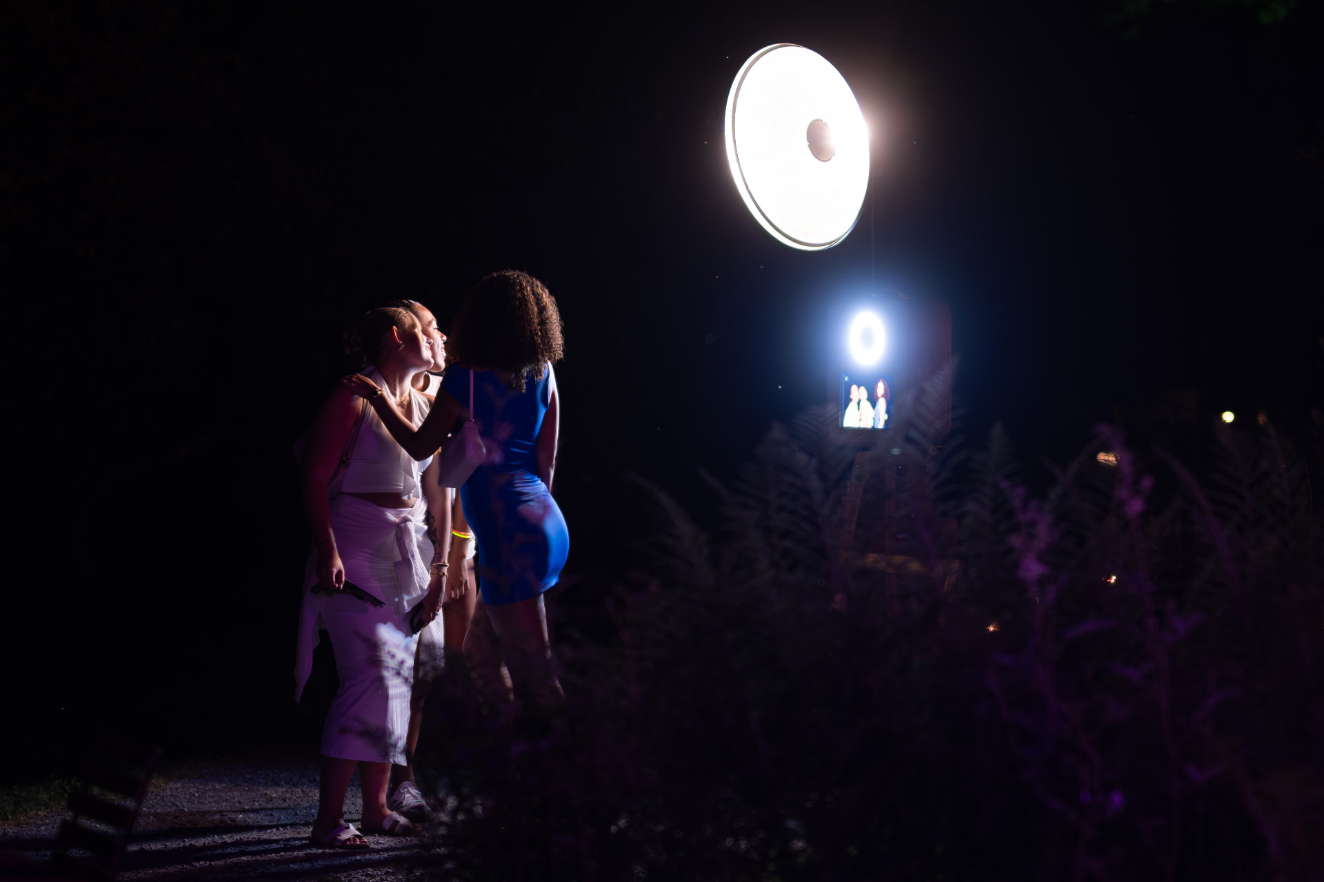 Drei Gäste posieren abends im Freien vor einer aufgebauten, beleuchteten Fotobox