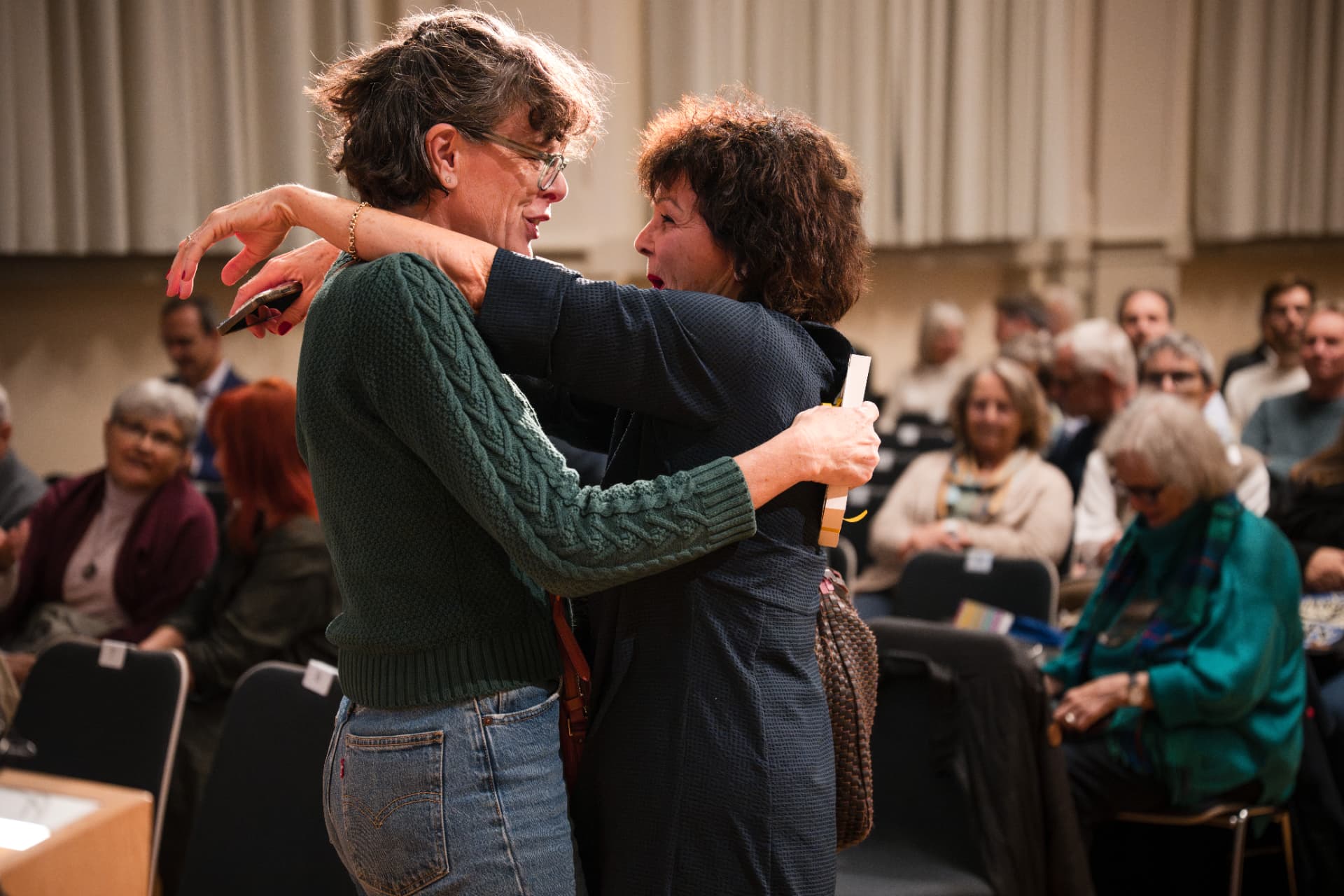 Zwei Frauen umarmen sich im Saal, im Hintergrund das Publikum