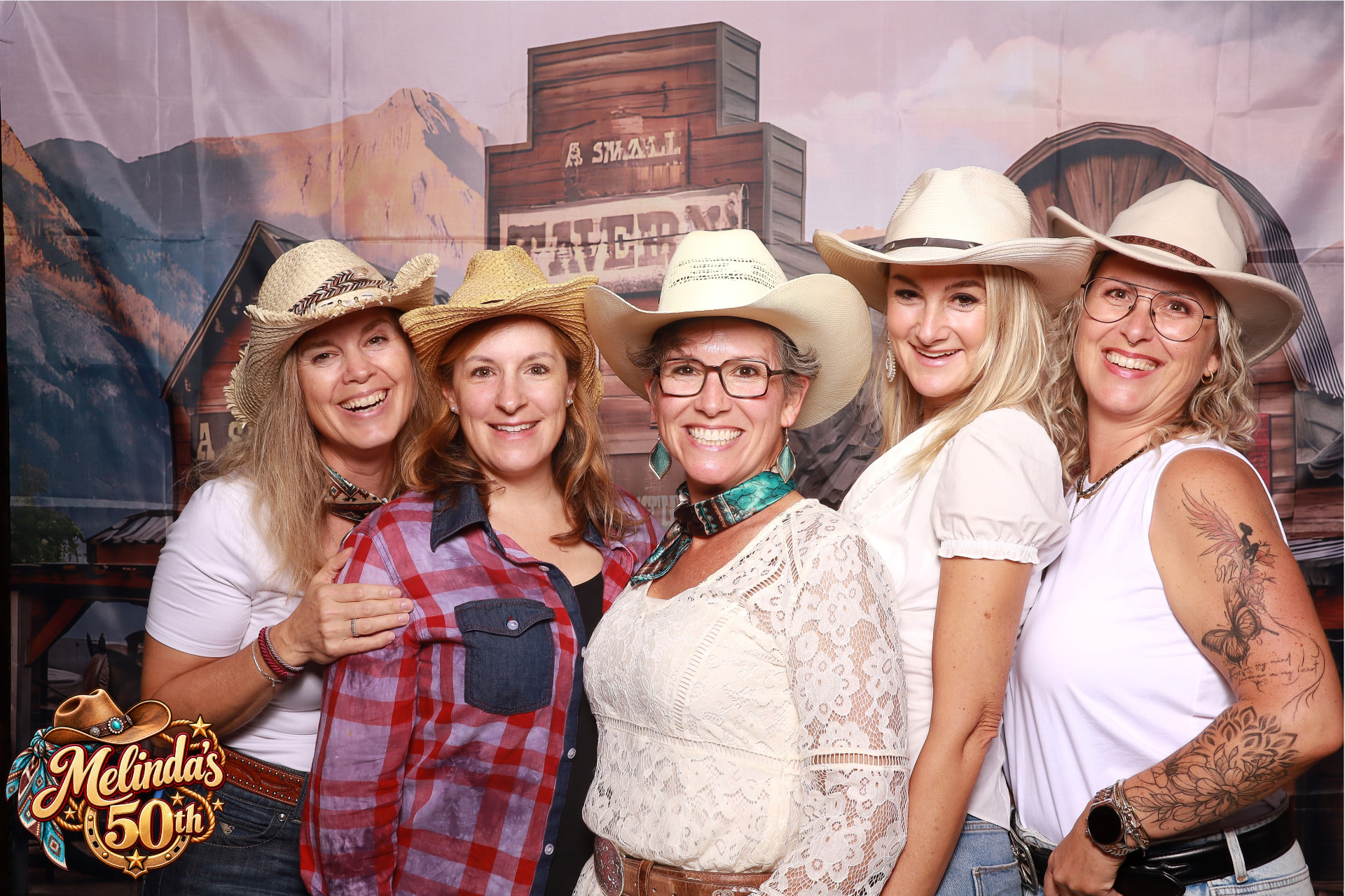 Fünf Gäste mit Cowboyhüten lachen vor einer Western-Kulisse in der Fotobox