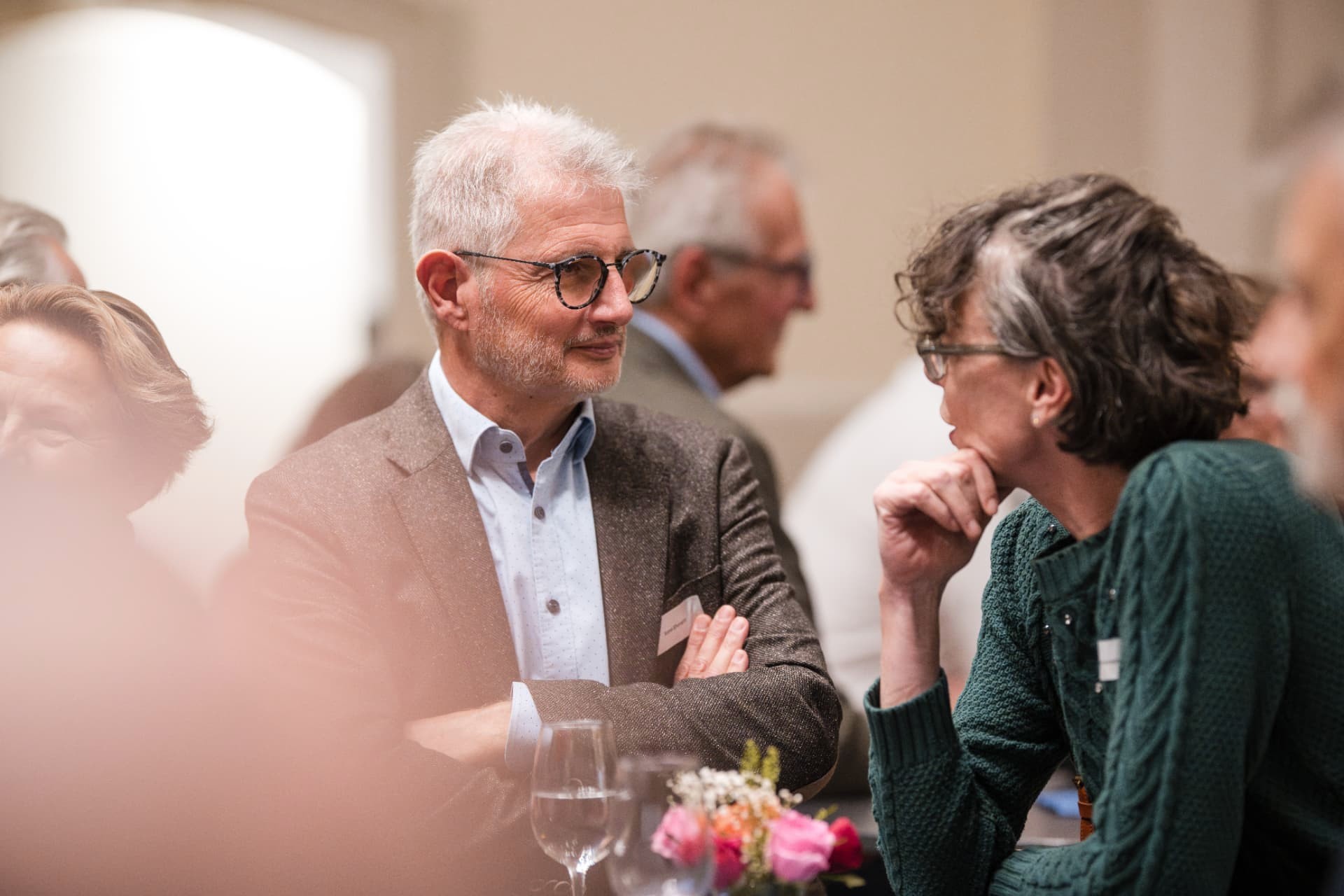 Guest at a laid table listening attentively to a woman in a green jumper