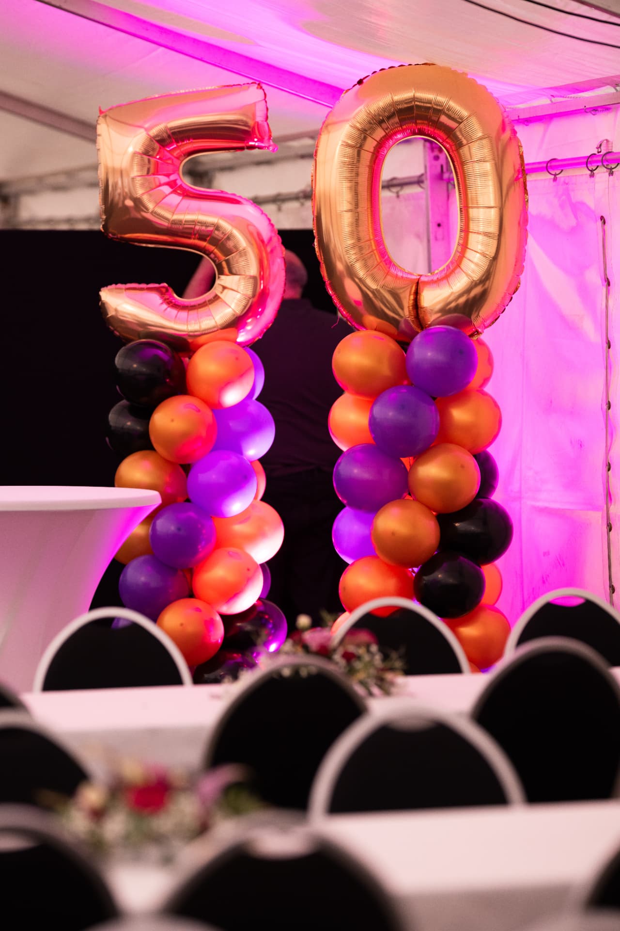 Goldene Zahlballons «5» und «0» auf zwei Ballonsäulen im magentafarbenen Festlicht