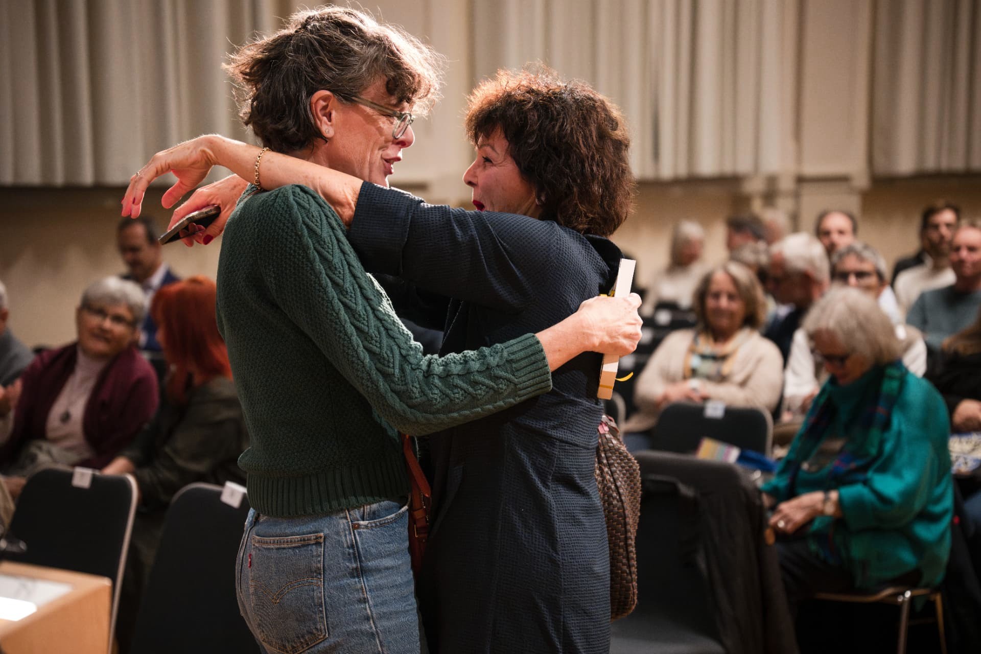 Two women embracing in the hall with the audience behind them