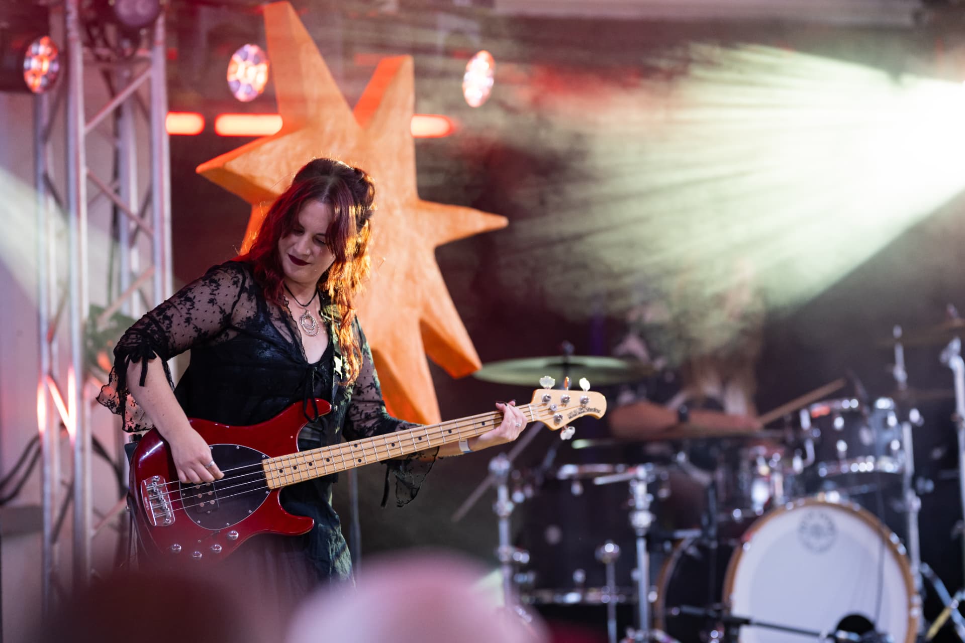 Gini Brown – Bassistin mit schwarz-roten Haaren spielt roten E-Bass, dahinter der Schlagzeuger im roten Gegenlicht
