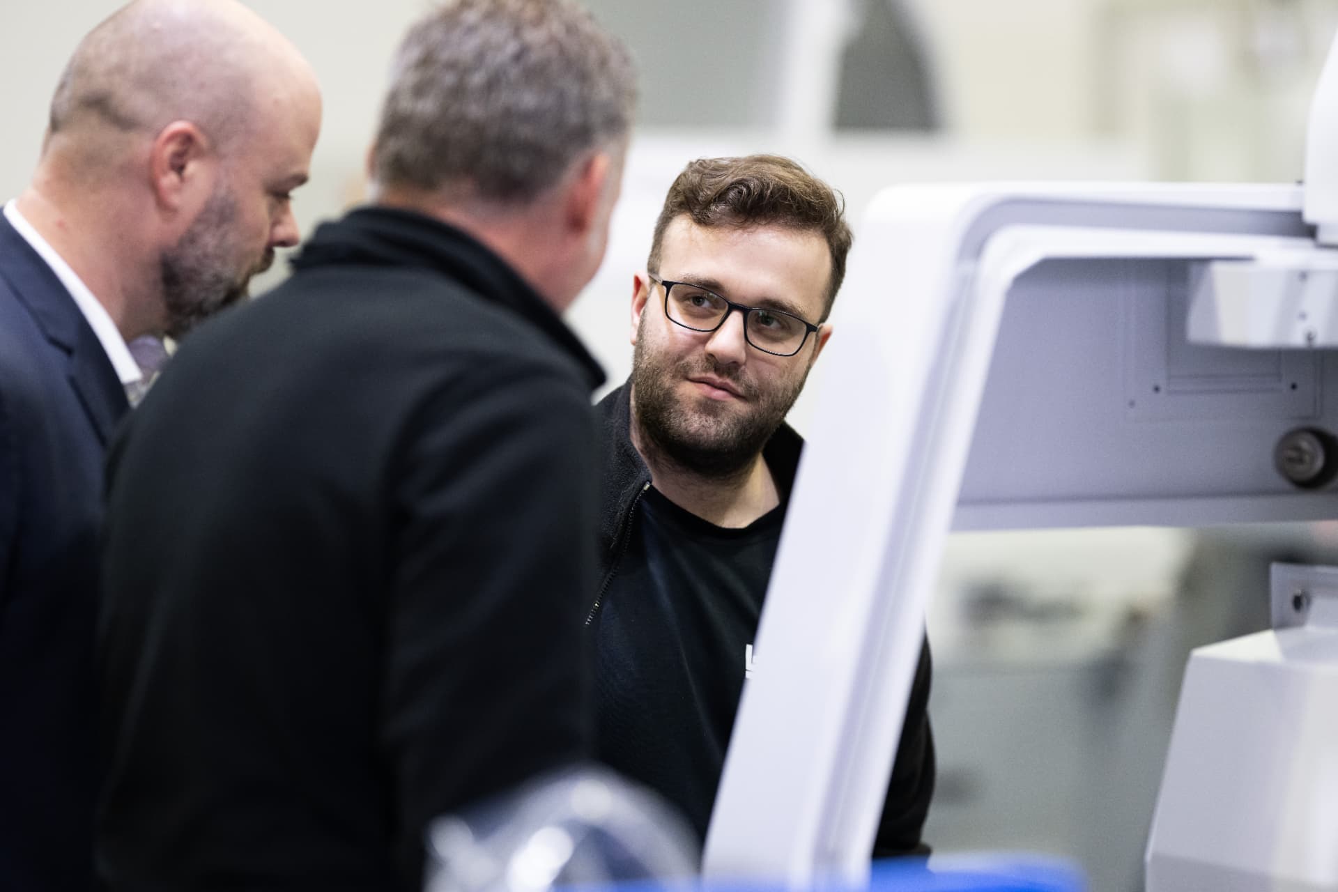 Dreiergruppe im fachlichen Gespräch an einer weissen Industriemaschine