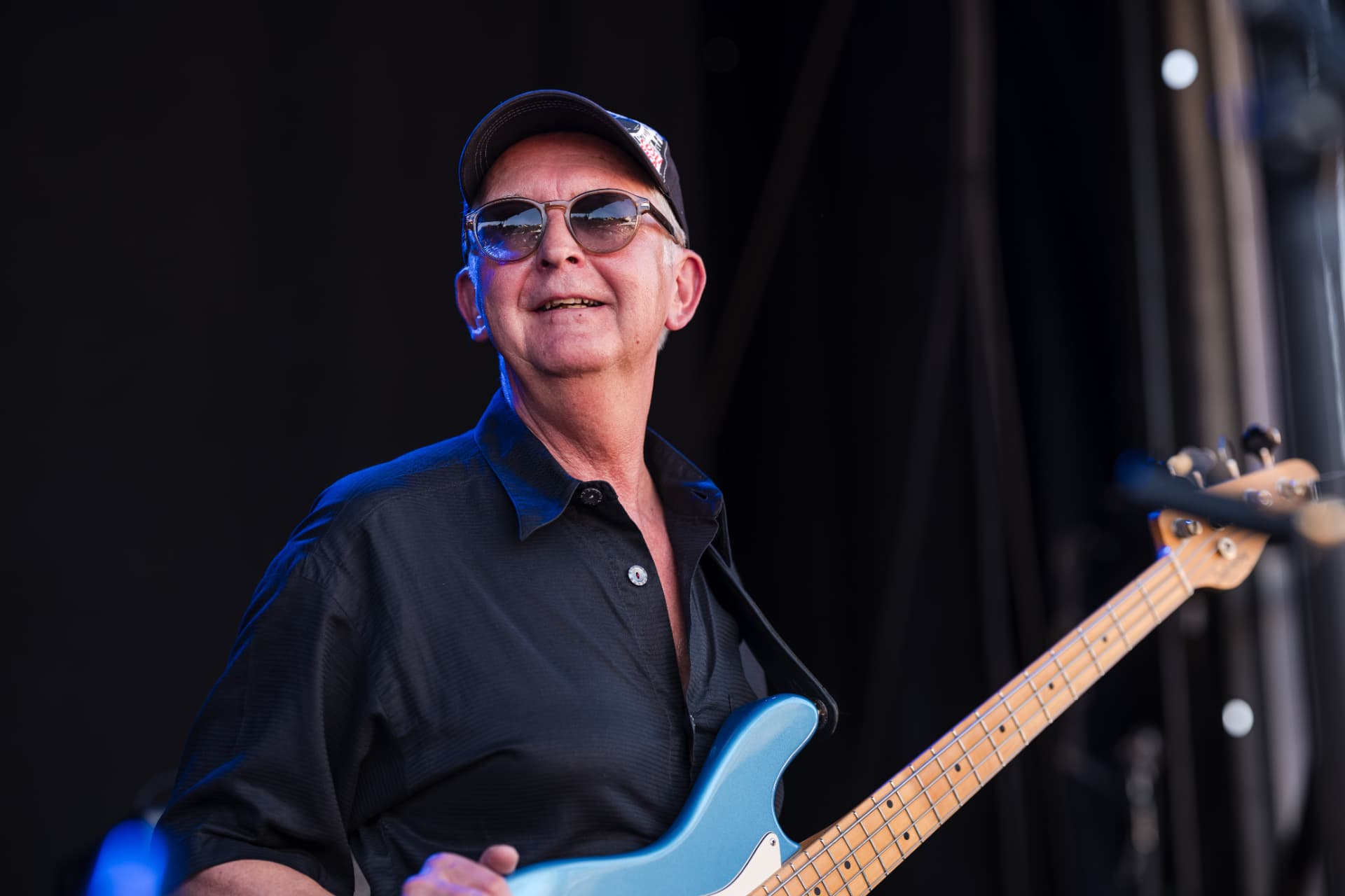 Bassist mit Cap und Sonnenbrille an der blauen Bassgitarre