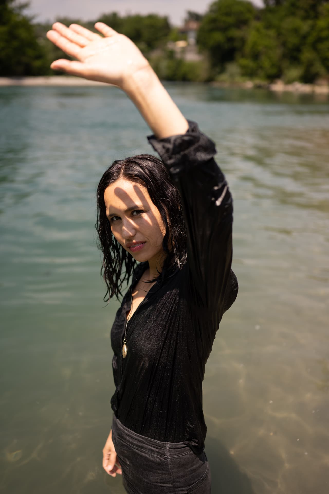 Meira Loom steht im Fluss im schwarzen Hemd, der erhobene Arm wirft einen Schatten auf ihr Gesicht