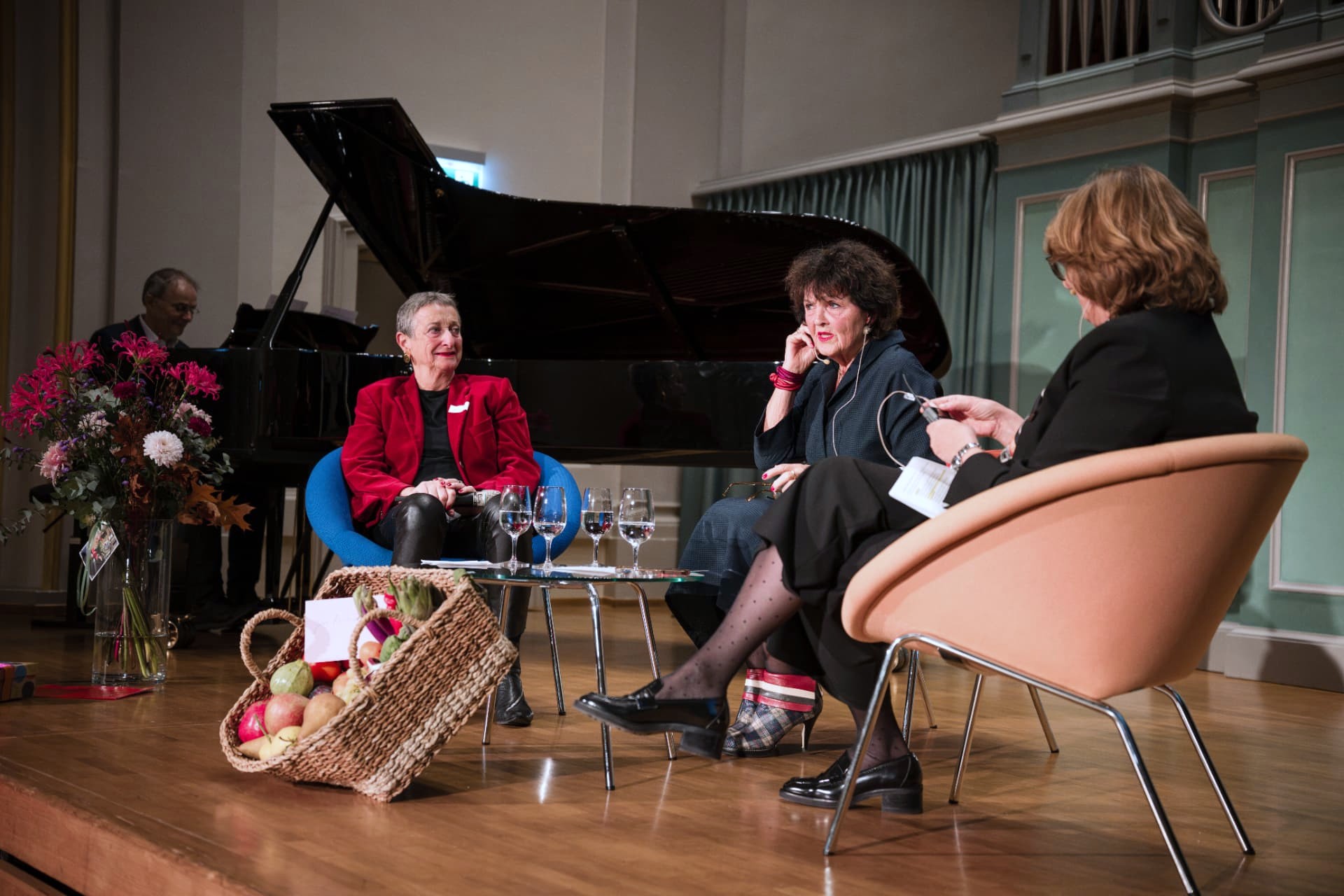 Panel discussion: three women seated in armchairs beside a grand piano and flowers