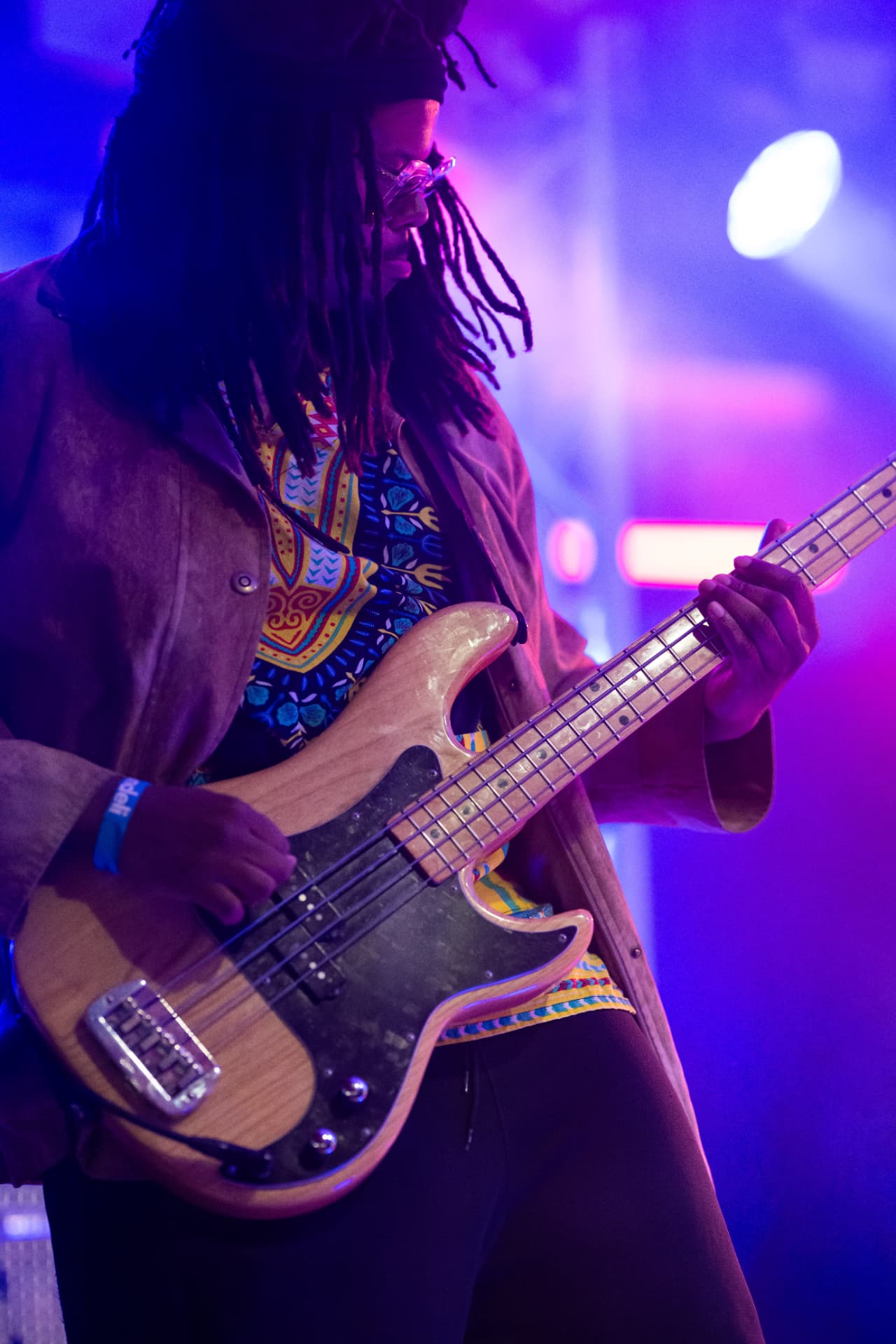 Captirando – Bassist mit Dreadlocks und Brille spielt einen hellen E-Bass im blau-violetten Licht
